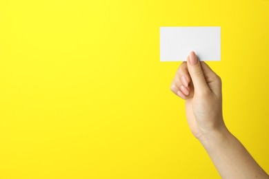 Woman holding blank business card on yellow background, closeup. Mockup for design