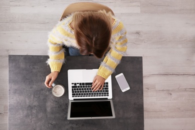 Woman working with laptop at table indoors, top view