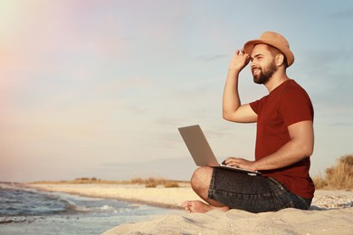 Photo of Man working with laptop on beach. Space for text