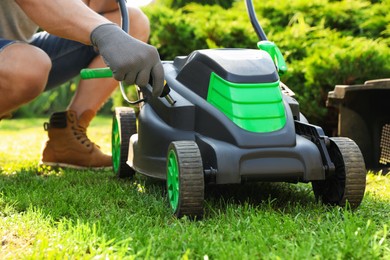 Photo of Young man with screwdriver fixing lawn mower in garden, closeup