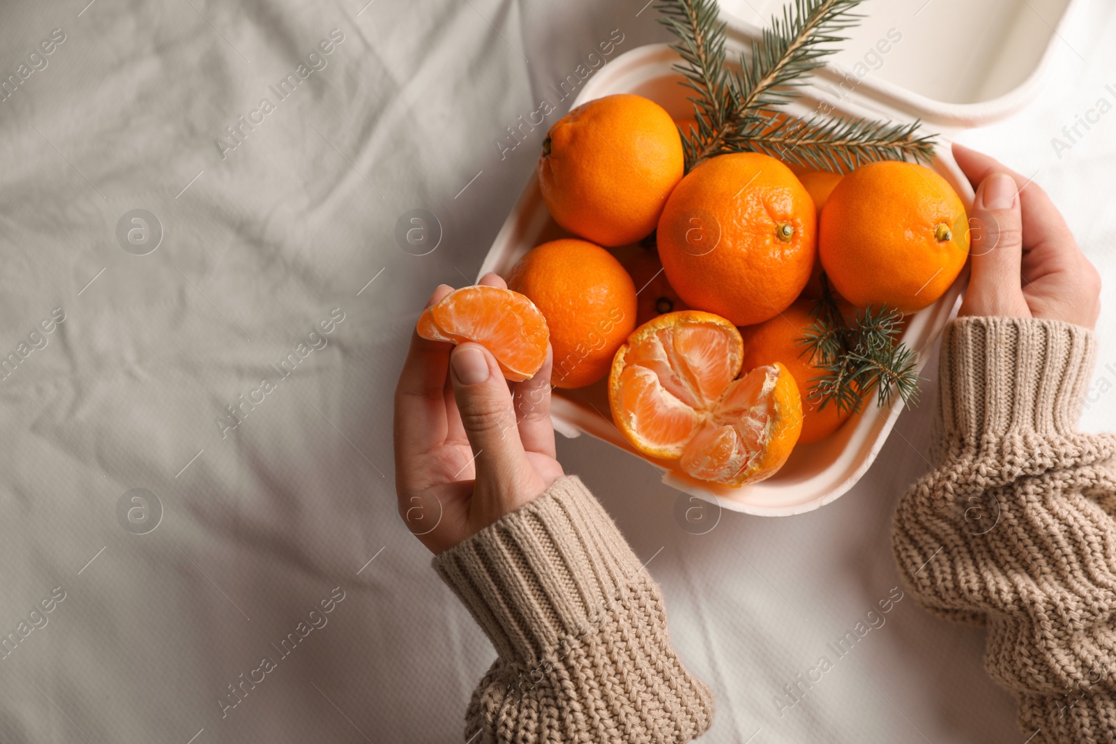 Photo of Woman with delicious ripe tangerines on white bedsheet, top view. Space for text