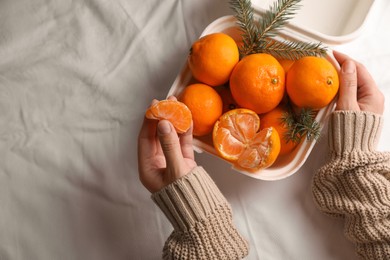 Woman with delicious ripe tangerines on white bedsheet, top view. Space for text