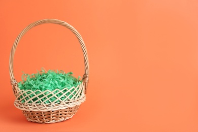 Photo of Easter basket with green paper filler on coral background, space for text