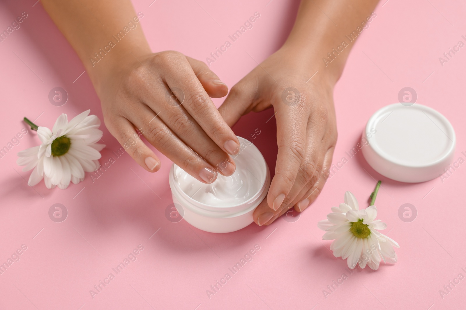 Photo of Woman with jar of hand cream and chamomile flowers on pink background, closeup