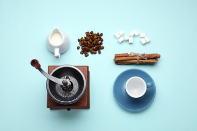 Flat lay composition with vintage manual coffee grinder and beans on light blue background