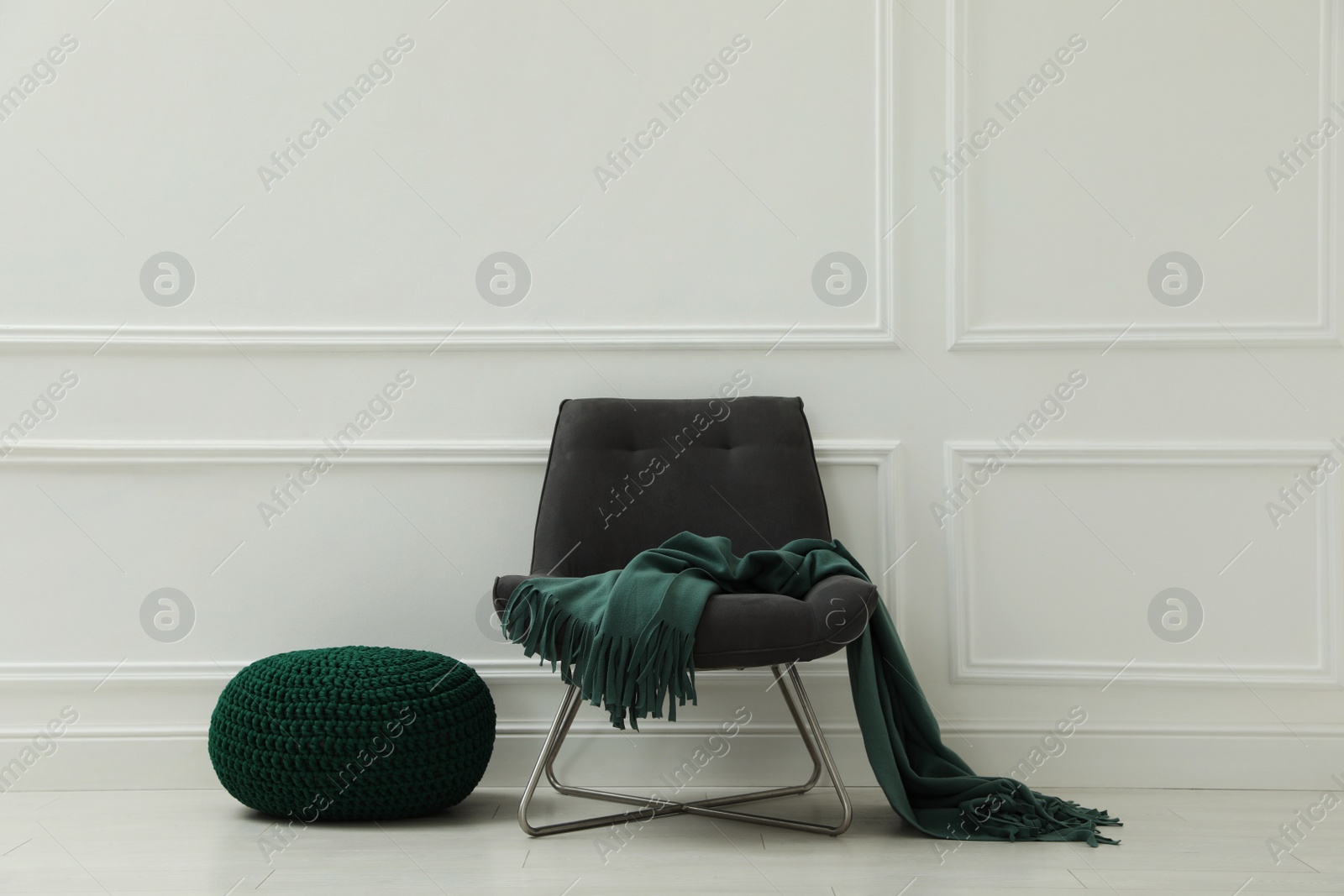 Photo of Knitted pouf and chair with plaid near white wall indoors. Space for text