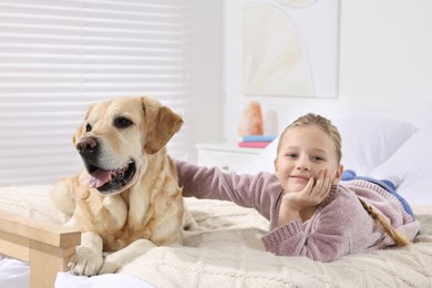 Photo of Cute child with her Labrador Retriever on bed at home. Adorable pet