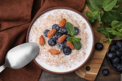 Tasty wheat porridge with milk, blueberries and almonds in bowl served on wooden table, flat lay