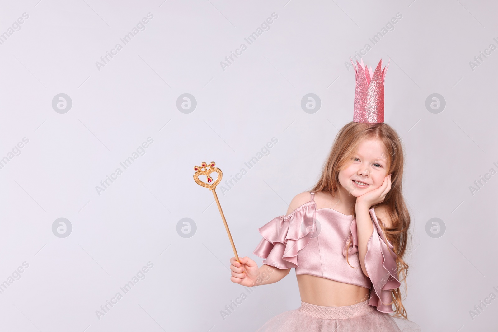 Photo of Cute girl in fairy dress with pink crown and magic wand on light grey background, space for text. Little princess