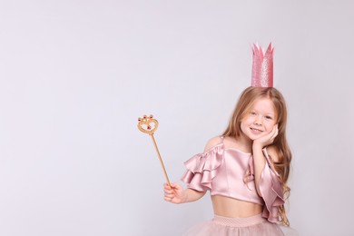Cute girl in fairy dress with pink crown and magic wand on light grey background, space for text. Little princess