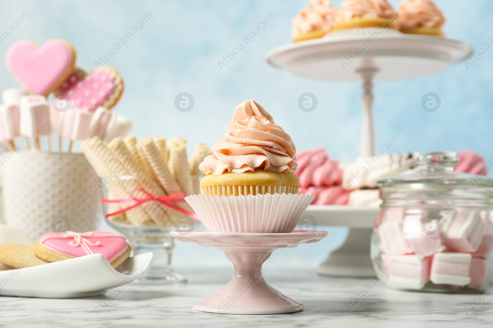 Photo of Stand with cupcake and other sweets on white marble table. Candy bar