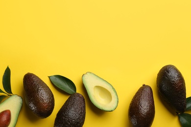 Photo of Whole and cut ripe avocadoes with green leaves on yellow background, flat lay. Space for text