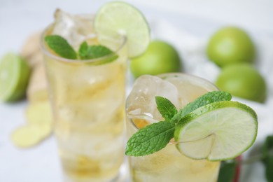 Glass of tasty ginger ale with ice cubes, lime slices and mint on blurred background, closeup. Space for text