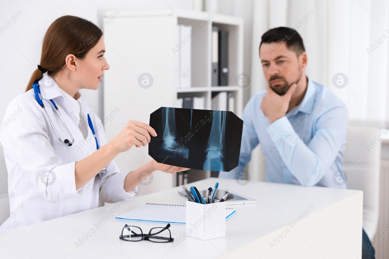 Photo of Orthopedist showing X-ray picture to patient at table in clinic