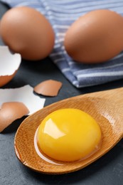 Photo of Wooden spoon with raw egg yolk on black table, closeup