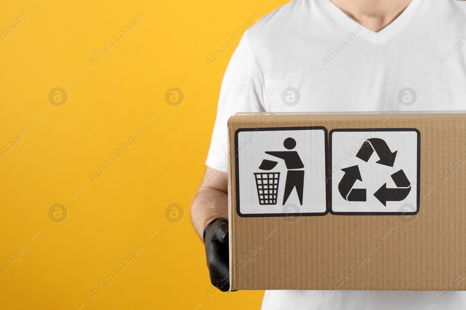 Photo of Courier holding cardboard box with different packaging symbols on yellow background, space for text. Parcel delivery