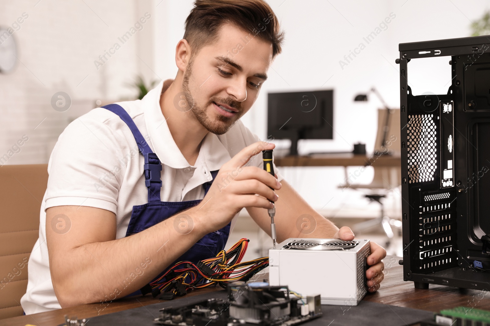 Photo of Male technician repairing power supply unit at table indoors