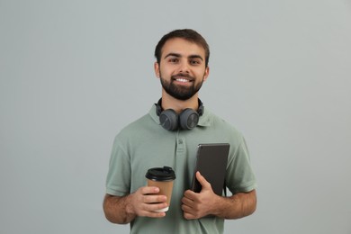 Photo of Student with headphones, tablet and paper cup of coffee on grey background