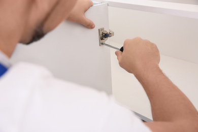 Photo of Worker installing door of kitchen cabinet, closeup