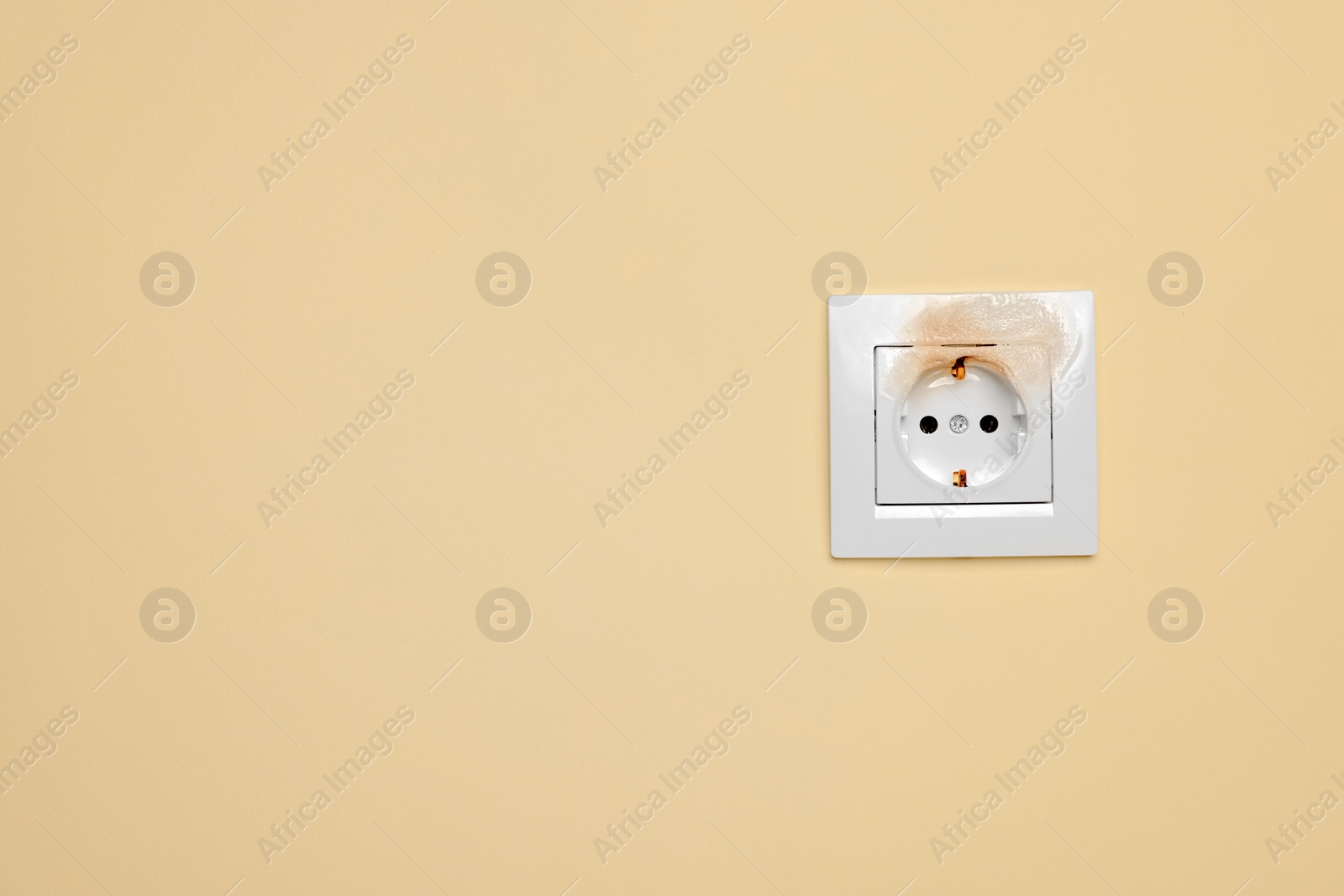 Photo of Burnt power socket on beige wall, space for text. Electrical short circuit