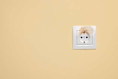 Burnt power socket on beige wall, space for text. Electrical short circuit