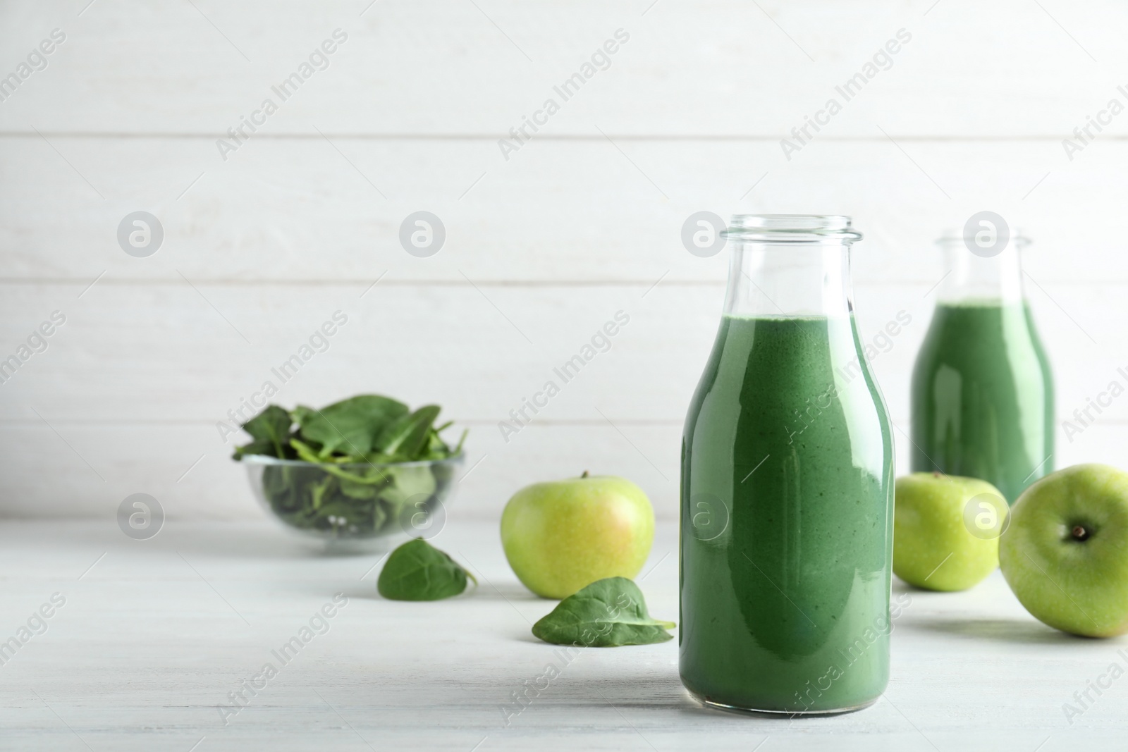 Photo of Composition with bottle of spirulina smoothie, spinach and fresh apples on table. Space for text