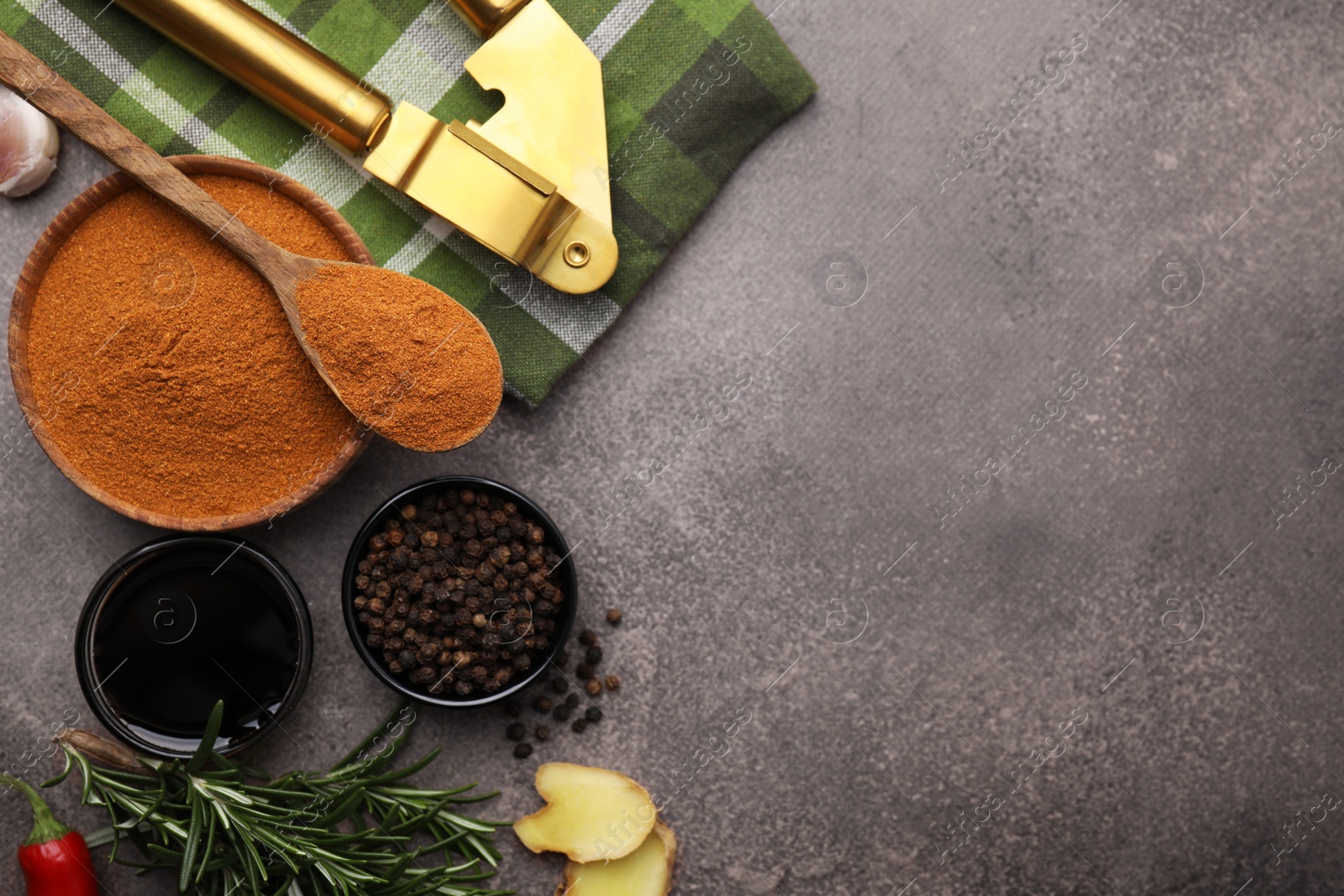 Photo of Aromatic spices, fresh ingredients for marinade and garlic press on brown table, flat lay. Space for text