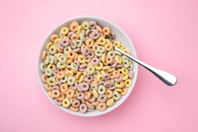 Photo of Tasty cereal rings in bowl and spoon on pink table, top view