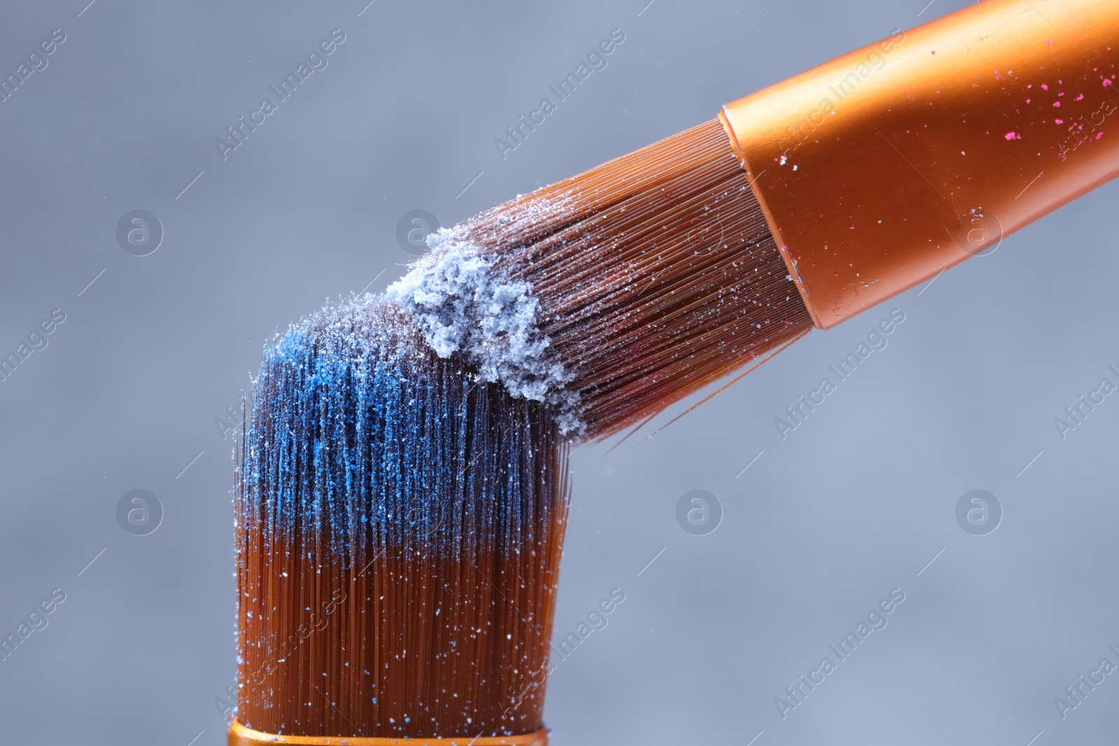 Photo of Makeup brushes with light blue eye shadows on grey background, macro view