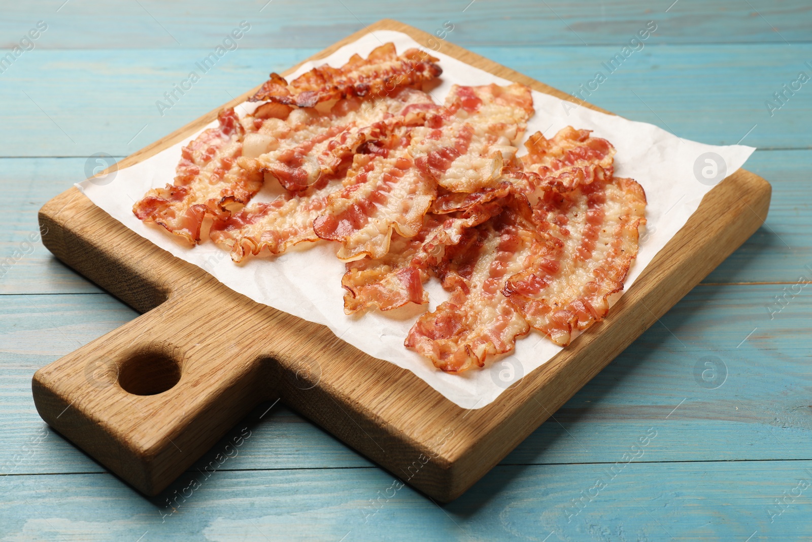 Photo of Delicious fried bacon slices on blue wooden table, closeup