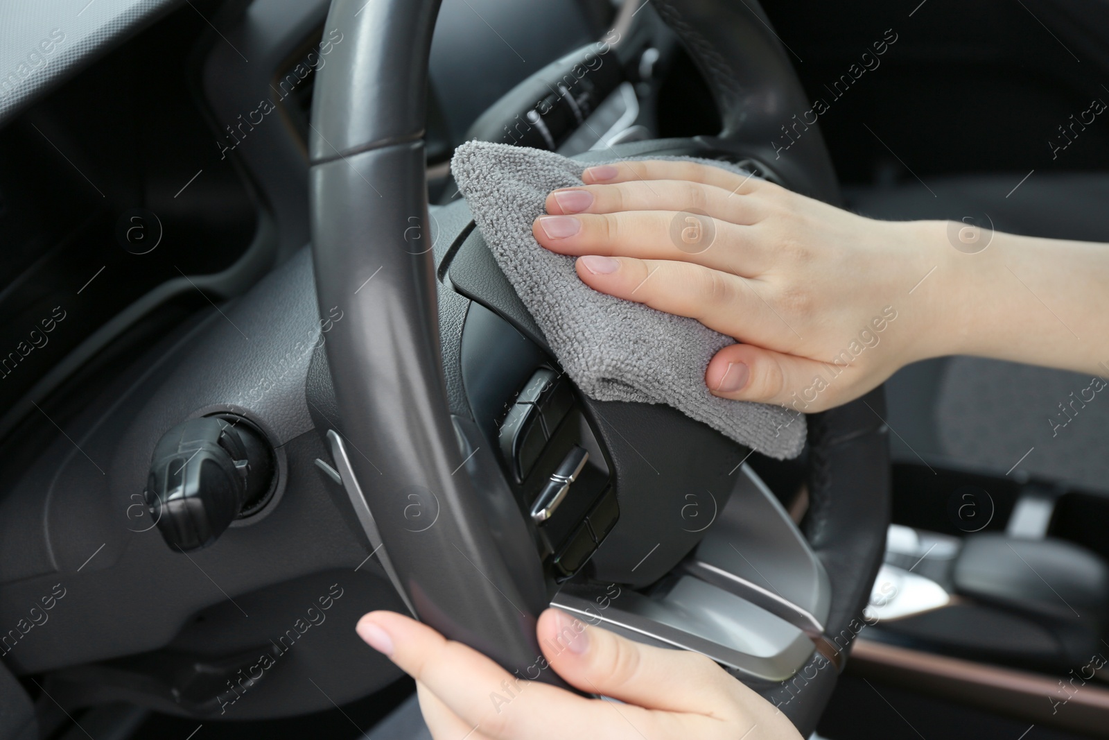 Photo of Woman cleaning steering wheel with rag in car, closeup