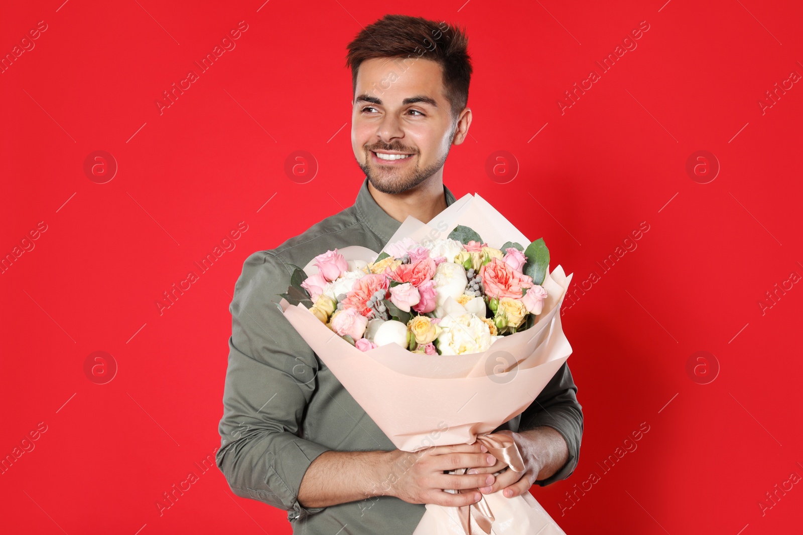 Photo of Young handsome man with beautiful flower bouquet on red background