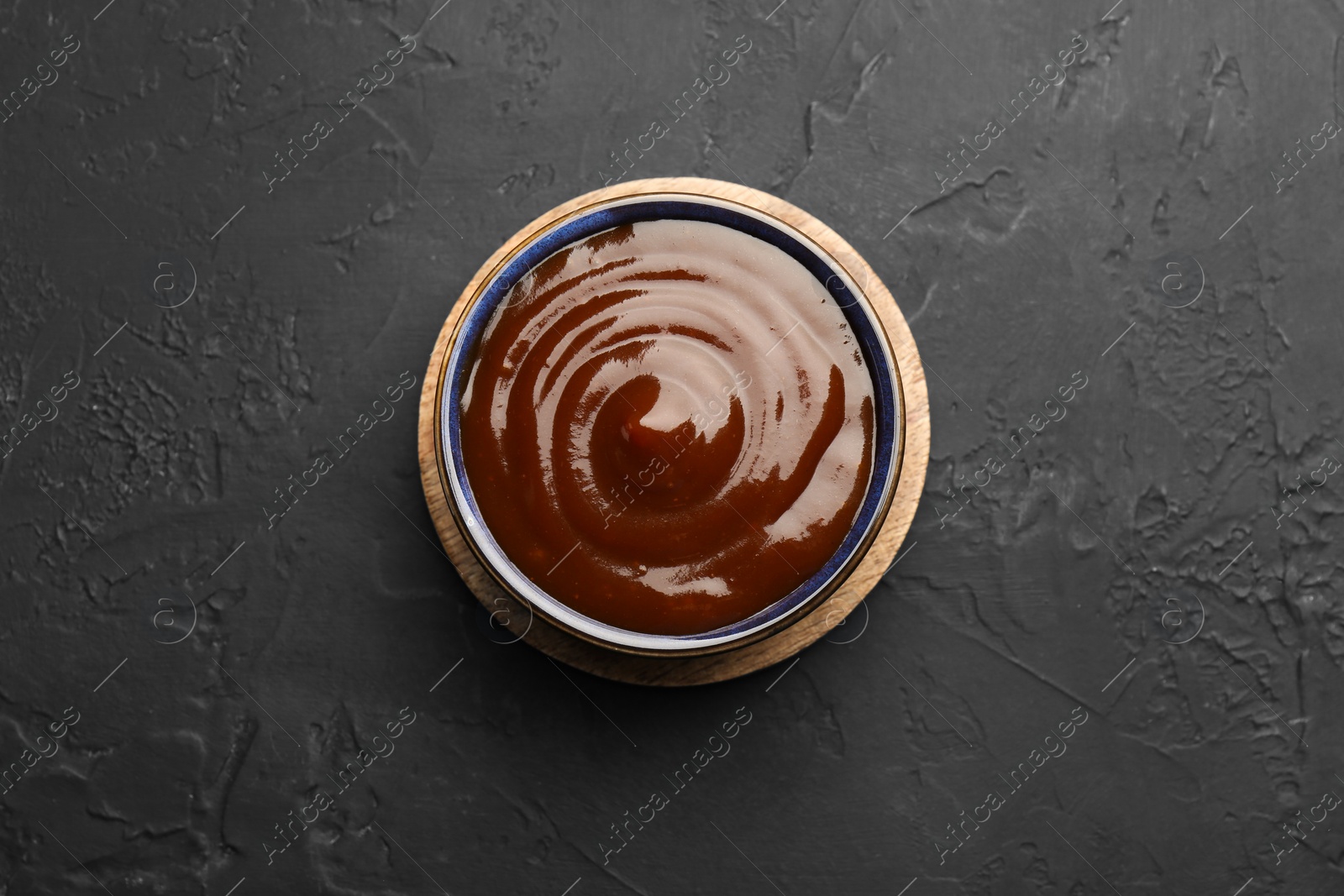 Photo of Tasty barbeque sauce in bowl on dark textured table, top view