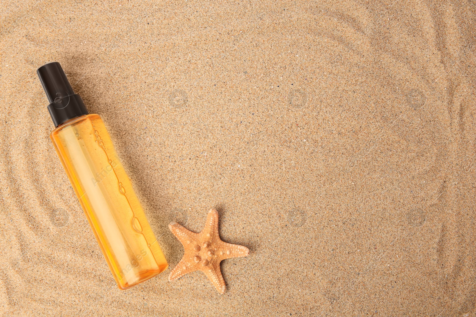 Photo of Bottle with serum and starfish on sand, top view with space for text. Cosmetic product