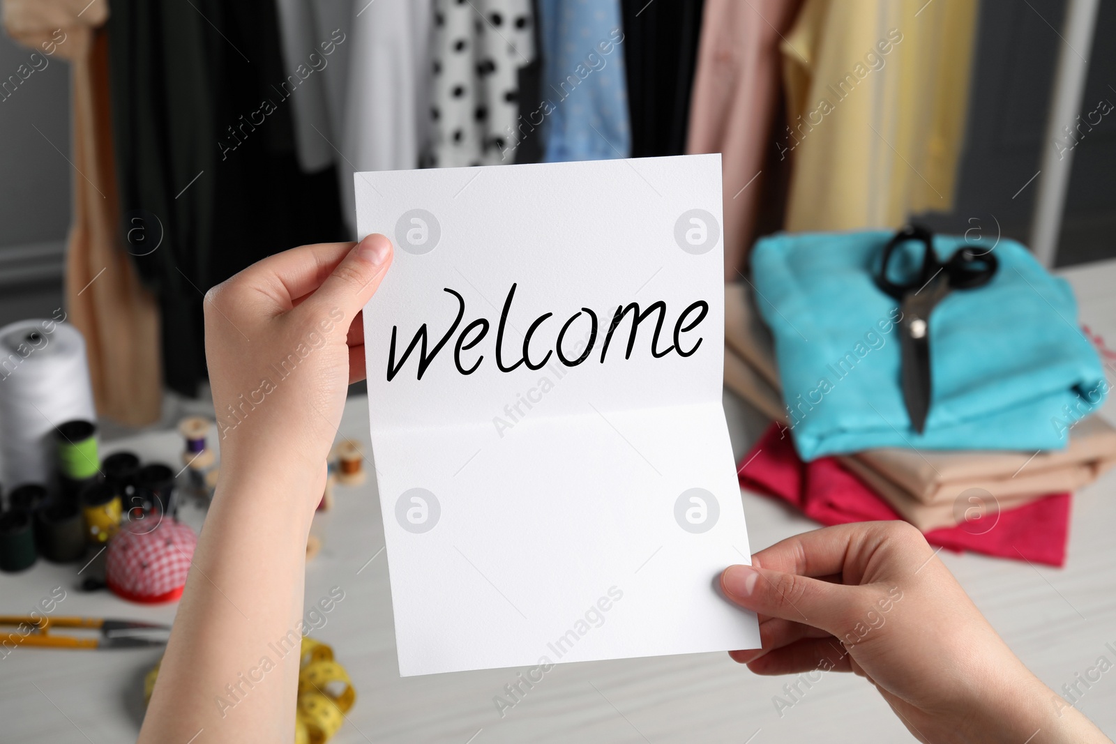 Image of Seamstress paper with word Welcome at table in atelier, closeup