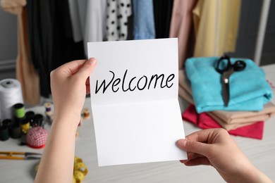 Seamstress paper with word Welcome at table in atelier, closeup