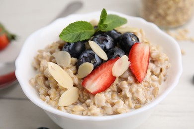 Photo of Tasty oatmeal with strawberries, blueberries and almond petals in bowl on white wooden table, closeup