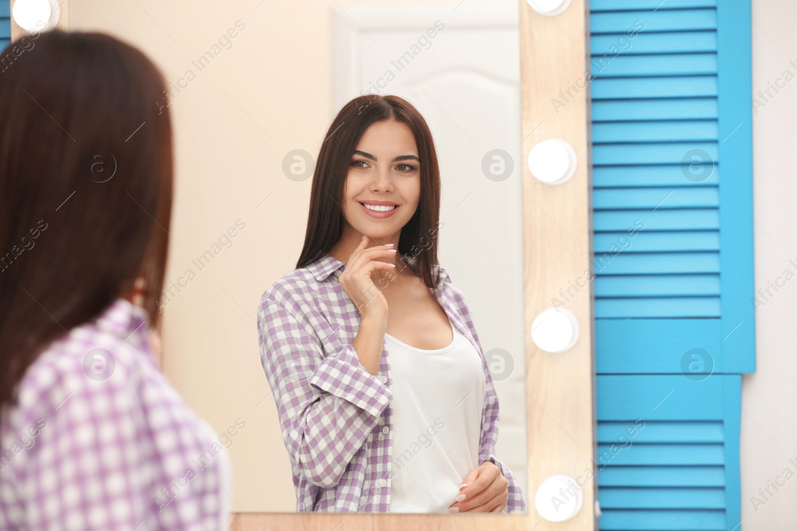 Photo of Young attractive woman looking at herself in stylish mirror at home