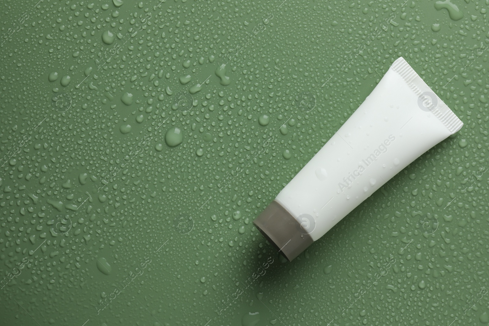 Photo of Moisturizing cream in tube on green background with water drops, top view. Space for text