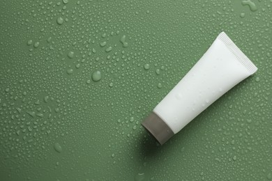 Moisturizing cream in tube on green background with water drops, top view. Space for text
