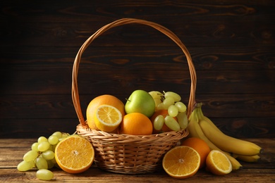 Photo of Wicker basket with different fruits on wooden table