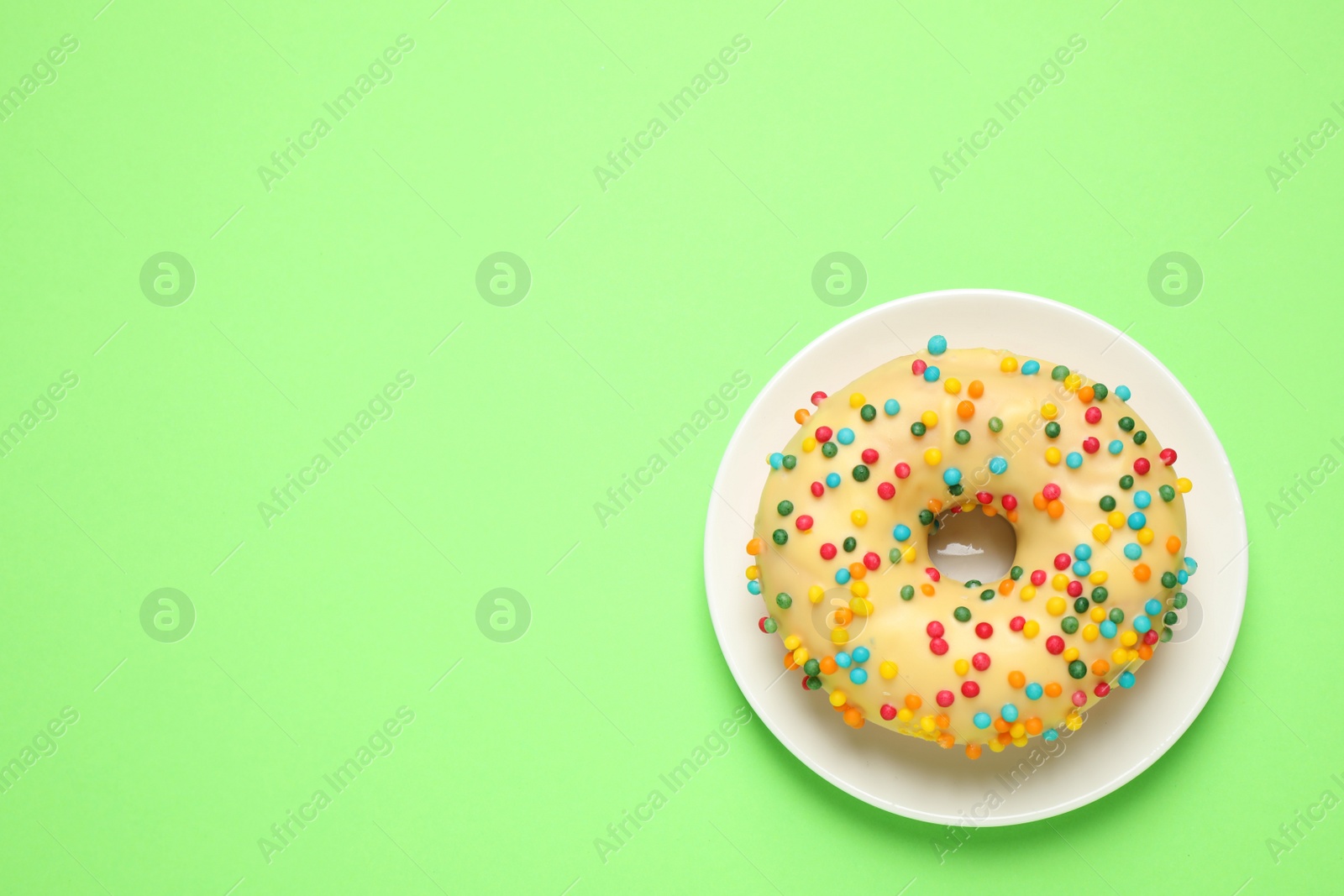 Photo of Delicious glazed donut on green background, top view. Space for text