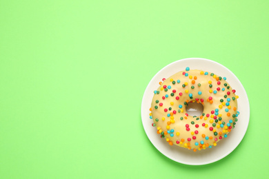 Photo of Delicious glazed donut on green background, top view. Space for text