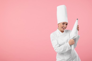 Happy professional confectioner in uniform holding piping bag on pink background. Space for text