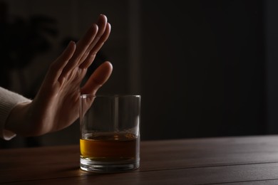 Photo of Woman refusing to drink whiskey at wooden table, closeup. Alcohol addiction