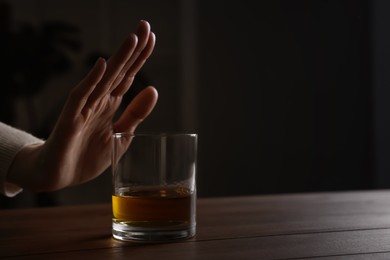 Woman refusing to drink whiskey at wooden table, closeup. Alcohol addiction