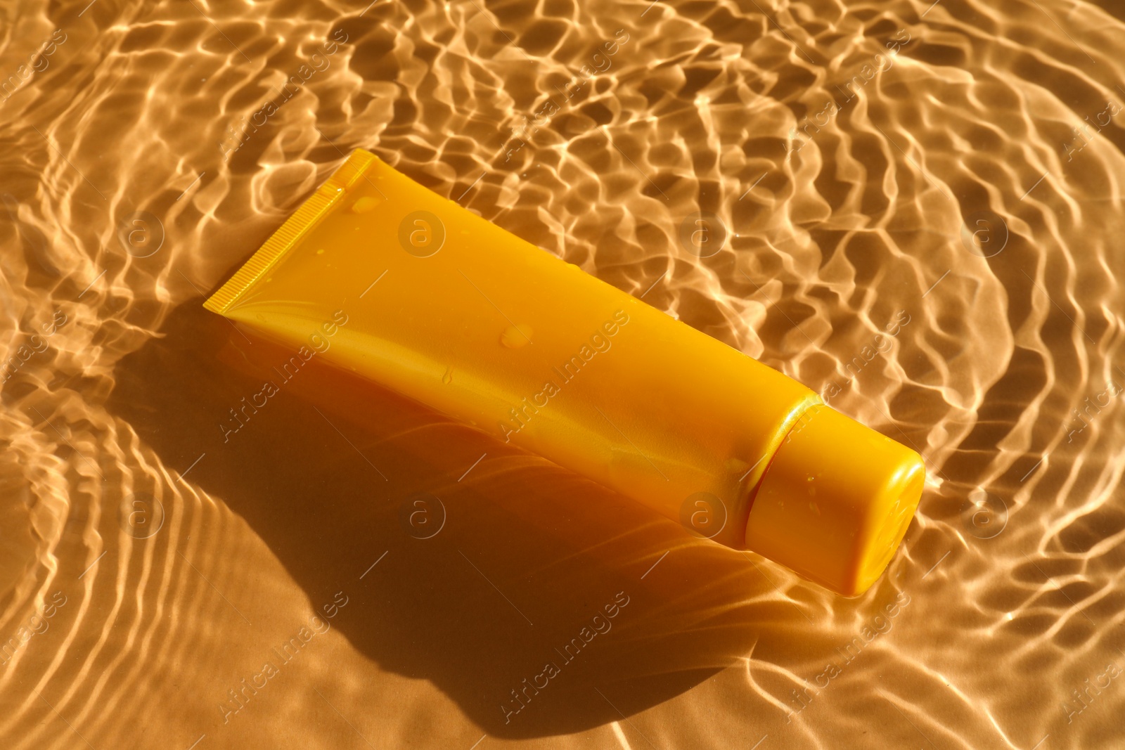 Photo of Tube with moisturizing cream in water on orange background