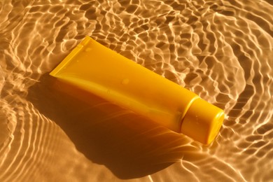 Photo of Tube with moisturizing cream in water on orange background