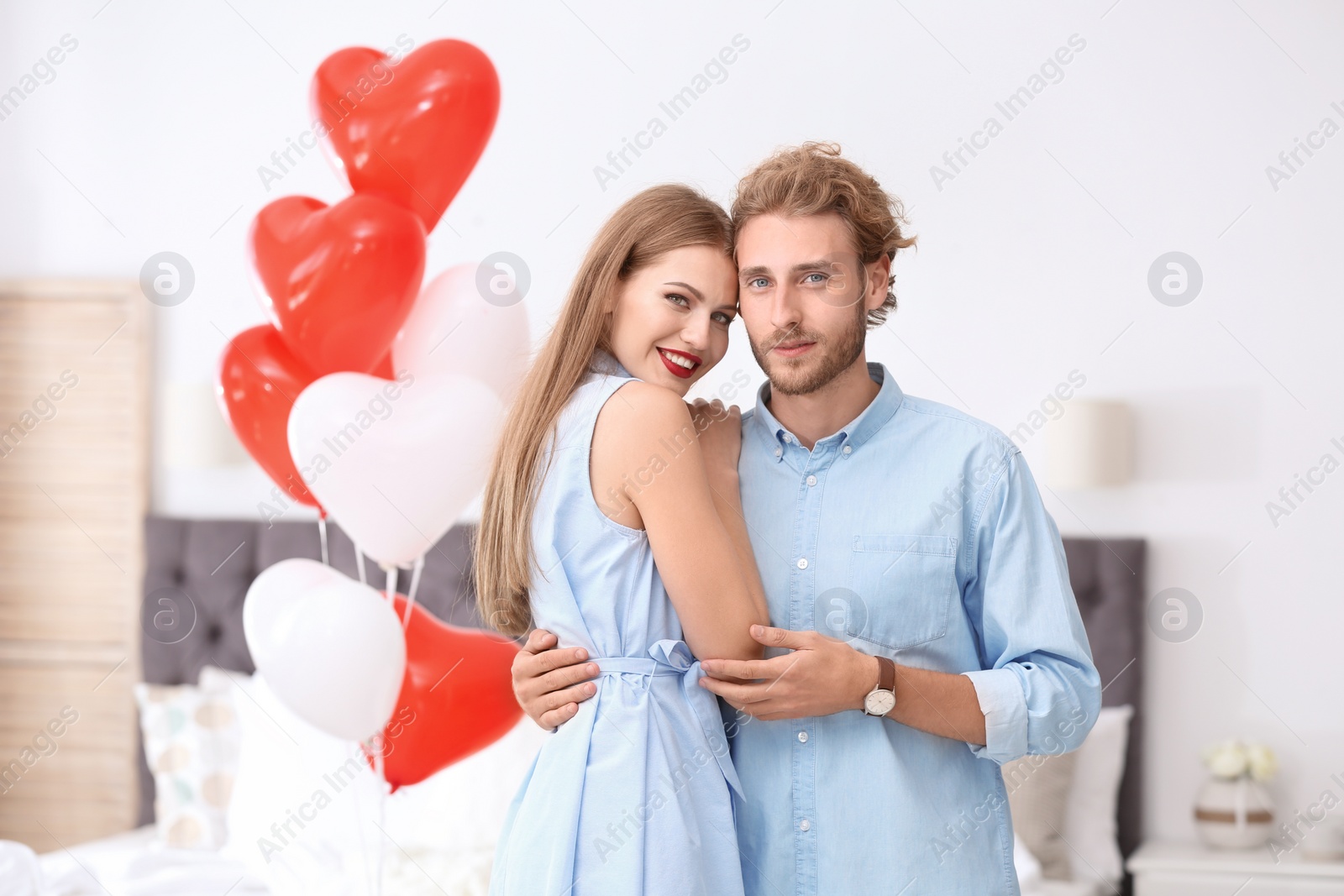 Photo of Young couple with air balloons in bedroom. Celebration of Saint Valentine's Day