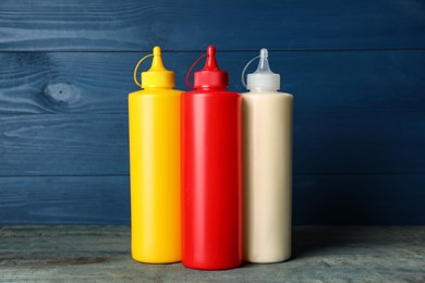Photo of Bottles of mustard, ketchup and mayonnaise on blue wooden table
